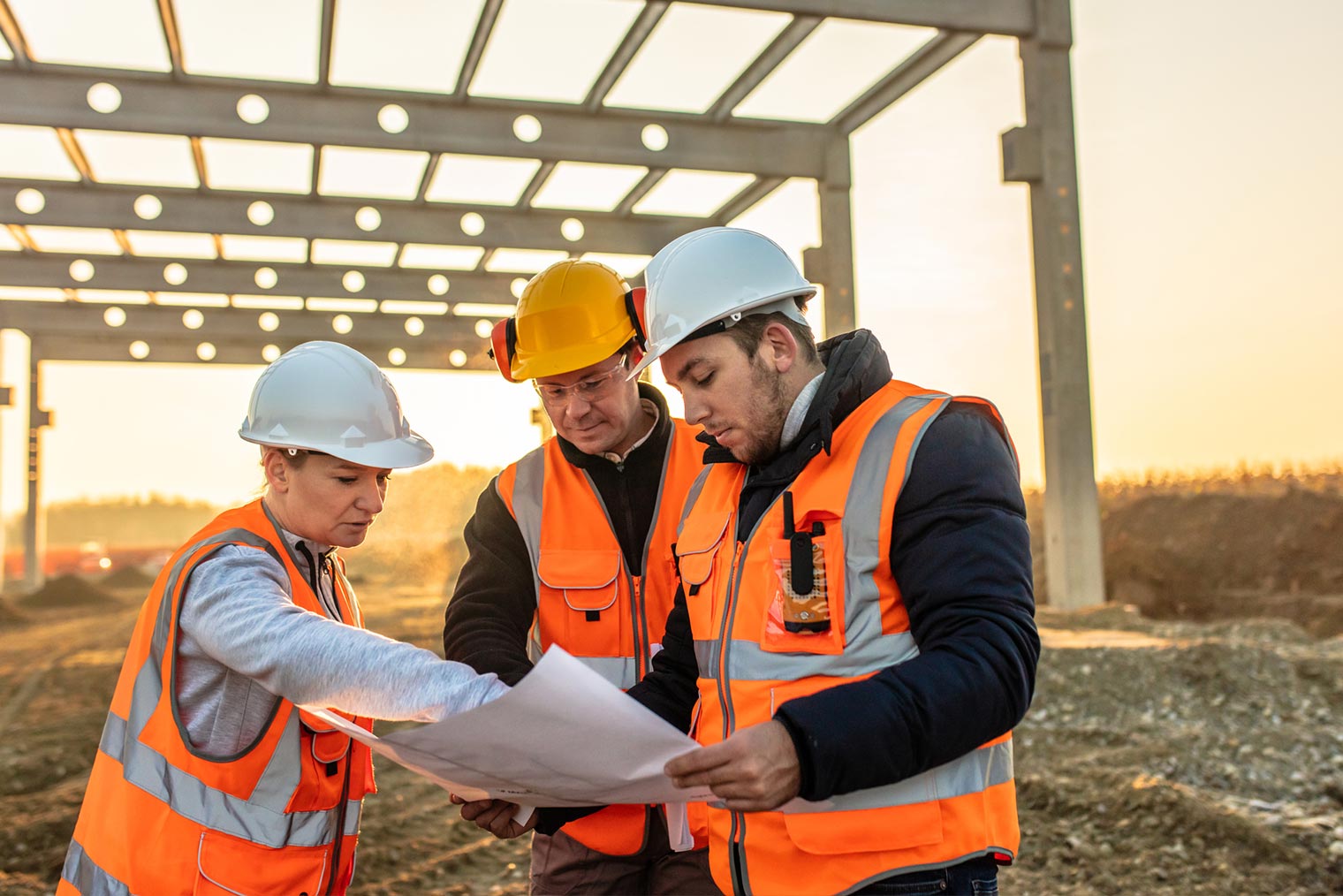 3 people wearing hard hats pointing at blueprint